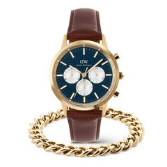 ブルーダイヤルとホワイトサブダイヤルが特徴のIconic Chronograph Pandaと、ゴールドのEllipse Cuban Chain Braceletを正面から撮影したセット全体の画像です。ブラウンレザーストラップの腕時計の手前にキューバンチェーンブレスレットを重ね、ゴールドトーンの統一感を演出しています。