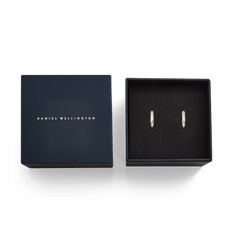 Daniel Wellington Arch Earrings Silverが、ネイビーのブランド専用ギフトボックスに収められた状態の俯瞰写真です。ブラックのクッション上にシルバーのフープピアスが左右に並び、ゴールドのロゴがあしらわれた蓋とともに、ギフトにふさわしい上品なパッケージングがご覧いただけます。