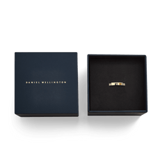 ダニエルウェリントン Classic Lumine Ring Gold 4mmを、ネイビーのブランドギフトボックスに収めた状態を真上から撮影した画像です。ボックスの蓋にはゴールドのブランドロゴが箔押しされており、黒いクッショントレーの上にクリスタル付きのゴールドリングが置かれています。