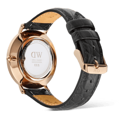 Classic Roman Numerals Date Black Croc Belly Rose Goldの裏蓋側を写した画像です。ポリッシュ仕上げのローズゴールドケースバックにはDaniel Wellingtonの刻印が入り、ブラッククロコベリーレザーストラップの型押し模様やキャメルカラーの裏地、ローズゴールドのピンバックルが確認できます。