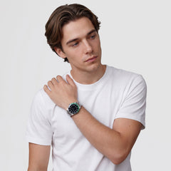 白いTシャツを着た男性がDaniel WellingtonのIconic GMT Linkを着用したスタイリング画像です。ブラックグリーンのセラミックベゼルとシルバーカラーのリンクブレスレットが、カジュアルな装いに洗練されたアクセントを加えています。