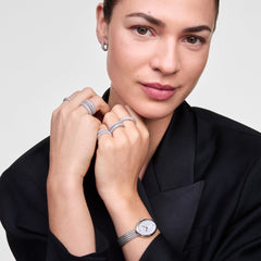 ブラックジャケットを着用した女性が、Juliette Braided Mesh White Sunray Silverを手首に合わせ、シルバーのリングやフープピアスとコーディネートしたスタイリング例です。編み込みメッシュのストラップとシルバーアクセサリーが、統一感のある上品な手元を演出します。