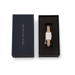 Daniel WellingtonのQuadro Crystal Zodiac Evergoldが、ネイビーのギフトボックスに収められています。ブラックのクッション上には、ゴールドメッシュストラップとクリスタルベゼルの腕時計が丁寧にセットされ、ケース下部には獅子座の星座チャームが添えられています。贈り物にぴったりの上品なパッケージです。