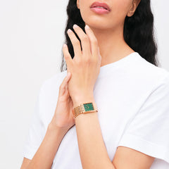 白いTシャツを着た女性がDaniel WellingtonのBound 9-Link Emerald Sunrayを着用している様子です。エメラルドグリーンのサンレイダイヤルとローズゴールドの9リンクブレスレットが手首に沿ってなめらかにフィットし、シンプルな装いに上品なアクセントを加えています。