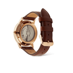 Iconic St Mawes Automatic Rose Goldの裏面をご紹介する画像です。サファイアガラスのエキシビションケースバック越しに、自動巻きムーブメントのローターや歯車を確認いただけます。ローズゴールドのケースバックにはモデル名やスペックが刻印されており、ブラウンレザーストラップのローズゴールドバックルにはブランドロゴが施されています。