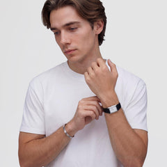 白いTシャツを着た男性が、Daniel WellingtonのLine Cuff Brushed Silverを右手首に着用し、左手首のレクタンギュラーウォッチと重ね付けしたスタイリング例です。ブラッシュ仕上げのシルバーカフが、さりげなく腕元を引き立てています。