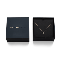 ダニエルウェリントンのネイビーギフトボックスに収められた、牡牛座モチーフのCrystal Zodiac Chain Necklace Goldの写真です。ブラックの内装にゴールドチェーンが映え、クリスタルをあしらった牡牛座のペンダントが中央に配置されています。隣にはブランドロゴ入りの蓋が添えられ、ギフトにぴったりの上品な仕上がりです。