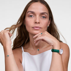 ローズゴールドとグリーンの統一感あるコーディネートを楽しむ女性のスタイリング写真。左手首にCrystalline Bezel Green Croc Rose Goldを着用し、グリーンストーンのネックレス、ピアス、リング、ブレスレットと合わせています。