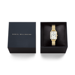 ネイビーカラーのブランドロゴ入りギフトボックスに収められたQuadro Roman Numerals Date 5-link Gold。黒いクッションケースの上に、ゴールドの5リンクブレスレットが丁寧にセットされています。贈り物にも最適なパッケージです。