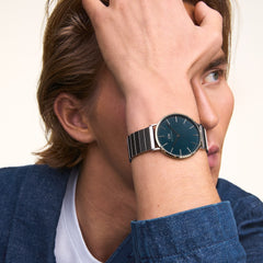 ダニエルウェリントン Classic Piano Link Arctic Silverを着用した男性のクローズアップ写真。ブルーのジャケットの袖口から覗くシルバーピアノリンクブレスレットと、深みのあるブルーダイヤルが自然光の下で上品な輝きを放っています。