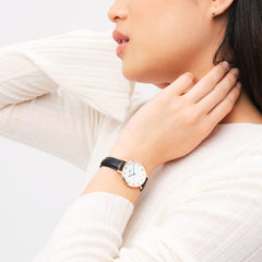 Petite Roman Numerals Sheffield ローズゴールドを着用した女性の手元。ホワイトのニットに合わせたブラックレザーストラップとローズゴールドケースが手首に自然になじみ、ブルースチールの針がさりげないアクセントとなっています。