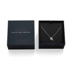 さそり座モチーフのCrystal Zodiac Chain Necklace Silverを、Daniel Wellingtonのネイビーブルーのギフトボックスに収めた俯瞰写真です。ブラックの台座中央に、クリスタルをあしらったさそり座のペンダントとシルバーチェーンが美しく配置されています。隣にはゴールドのブランドロゴが入った蓋が添えられています。