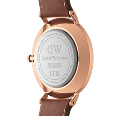 Classic Multi-Eye St Mawes Amber Rose Goldの裏蓋をクローズアップした画像です。ローズゴールドケースの背面にはDaniel Wellingtonのロゴとシリアルナンバーが刻印されており、ステンレススチール素材と3ATM防水仕様が確認できます。ダークブラウンのレザーストラップがラグに取り付けられています。