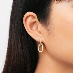 ダニエルウェリントン Crystal Link Earrings Goldを身に着けた女性の耳元をクローズアップ。ゴールドのフープからキュービックジルコニアが輝くオーバルリンクが揺れ、黒髪とのコントラストが上品なアクセントを添えています。