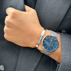 ダークグレーのスーツに合わせたClassic Mesh Arcticの着用イメージです。ブルーのダイヤルとシルバーメッシュのストラップがビジネススタイルに自然に馴染み、Daniel Wellingtonのシルバーバングルとの重ね付けもおすすめです。
