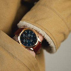 Iconic Chronograph St Mawes Arctic Rgを着用したスタイリングイメージです。キャメルのボアジャケットの袖口から、ブルーサンレイのダイヤルとダークブラウンのレザーストラップがのぞき、ローズゴールドのケースが暖色系のコーディネートに自然になじんでいます。