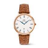 Daniel Wellington Classic Roman Numerals Dateの正面プロダクト画像。ホワイト文字盤にローマ数字のインデックスとディープブルーの針、6時位置に日付窓を配したローズゴールドケースに、クロコダイル型押しのライトブラウンレザーストラップを合わせたデザインです。