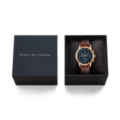 Daniel Wellingtonのギフトボックスに収められたIconic Chronograph St Mawes Arctic Rg。ネイビーカラーのパッケージに、ブルーのダイヤルとダークブラウンのレザーストラップをあしらった腕時計がクッションの上にセットされています。贈り物にぴったりの上品な仕上がりです。