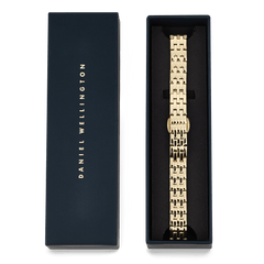 Daniel Wellington 5-Link Strap Goldが、ネイビーのブランド専用ボックスに収められています。ポリッシュ仕上げの5列ゴールドリンクが黒いクッションカバーの上に整然と並び、ギフトにも最適な上品なパッケージです。