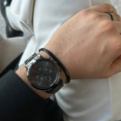 白いトップスに黒のジャケットを合わせた男性の手首に、Iconic Chronograph Link Onyx Bが映えています。ブラックのリンクブレスレットとサンレイ仕上げの文字盤が、日常のコーディネートにすっきりと馴染み、黒のリングやバングルとの重ね付けスタイルもおすすめです。