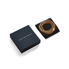 Daniel WellingtonのChunky Chain Necklace Goldを、ブランドロゴ入りのネイビーギフトボックスとブラックのスエード調ポーチとともに並べたパッケージ写真です。ゴールドのチェーンがポーチの上で円を描くように収まり、贈り物にぴったりの上品な仕上がりとなっています。