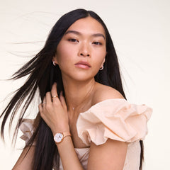 Daniel Wellington Pavé Crystal Earrings Rose Goldを身に着けた女性のスタイリングイメージです。クリスタルの輝きが美しい小ぶりなローズゴールドのフープピアスを、同系色のネックレスやリング、ローズゴールドの腕時計と合わせ、統一感のあるコーディネートに仕上げています。