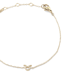 牡牛座モデルのCrystal Zodiac Chain Bracelet Goldを斜め上から撮影したクローズアップ画像です。ゴールドの繊細なチェーンが優雅な弧を描き、中央下部にはクリスタルをあしらった牡牛座のシンボルが輝いています。右上にはロブスタークラスプ、左上にはブランド刻印プレートが確認できます。