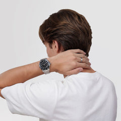 白いTシャツを着た男性がIconic GMT Link Black Ceramic Bezel Silverを身に着け、首の後ろに手を添えたポーズをとっています。シルバーのリンクブレスレットとブラックセラミックベゼルが手元で存在感を放ち、シンプルなリングとのコーディネートが映えています。