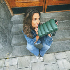 デニムコーディネートの女性が石段に座り、Sadie Bag Green Sを手にしたスタイリングイメージです。縦パフ加工のグリーンレザーがカジュアルな装いに上品なアクセントを添えています。