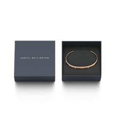 Daniel WellingtonのClassic Lumine Bracelet ローズゴールドが、ネイビーのギフトボックスに収められています。ブラックのクッションケースにクリスタル付きのオープンカフが丁寧に配置され、贈り物にぴったりの上品なパッケージです。