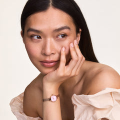 Petite Mini Blush Melroseを着用した女性のポートレートです。ブラッシュピンクのオフショルダートップに合わせ、ローズゴールドのメッシュストラップとピンクダイアルがブレスレットのように手首に馴染んでいます。
