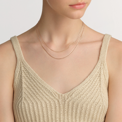 Daniel WellingtonのFlat Chain Necklace RGを別のチェーンネックレスと重ね付けした着用例です。ベージュのVネックニットの胸元で、ローズゴールドの2本のチェーンがデコルテに沿い、繊細なレイヤードスタイルを演出します。