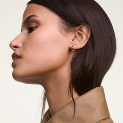 ダニエルウェリントンの3-Link Earrings Goldを着用した女性の横顔クローズアップ。小ぶりなゴールドのフープピアスが耳元で控えめに輝き、ベージュのトップスと調和した上品なコーディネートです。