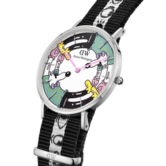 Steven Harrington x Daniel Wellingtonの限定コラボモデルを斜めから捉えたダイヤルのクローズアップです。ピンク、イエロー、ミントグリーンのポップなキャラクターが文字盤の外周を彩り、ピンクの針がアートの中心で時を刻みます。シルバーポリッシュのケースと、アイモチーフがあしらわれたブラックのNATOストラップの質感もご確認いただけます。