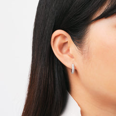 ダニエルウェリントンのPavé Crystal Earrings Silverを着用した女性の耳元をクローズアップ。クリスタルがあしらわれた小ぶりなシルバーフープピアスが、黒髪の間から光を受けて繊細に輝きます。