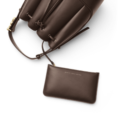 Lewis Bag Brownに付属するDaniel Wellingtonのロゴ入りポーチをクローズアップした画像です。バッグ本体のドローストリング部分にストラップで取り付けられたポーチが手前に広がり、同系色のブラウンエコレザーにはゴールドの箔押しロゴが上品にあしらわれています。