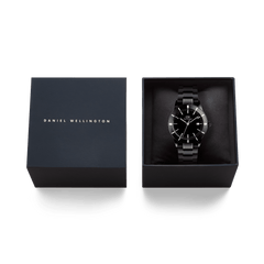 ダニエルウェリントンのブランドロゴがあしらわれたネイビーカラーのギフトボックスに収められた「Iconic Paradigma Link Black」。クッションの上にオールブラックの本体が丁寧にセットされており、贈り物としてそのままお届けできる仕様です。