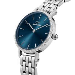 Petite Lumine Bezel 5-Link Arcticを斜めからクローズアップした画像です。深みのあるアークティックブルーのサンレイダイヤルに放射状の輝きが映え、ベゼルにあしらわれたクリスタルの煌めきとシルバーカラーの5リンクブレスレットの細部まで確認できます。