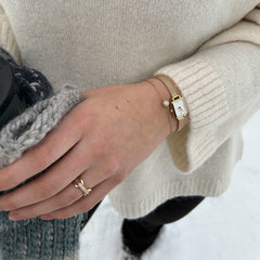 Quadro Miniのゴールドメッシュ腕時計とPavé Crystal Braceletを重ね付けした着用イメージです。クリーム色のニットの袖口から覗くスクエア型の腕時計と、パヴェクリスタルのチャームが揺れるゴールドチェーンブレスレットが、冬のコーディネートに上品な華やかさを添えます。
