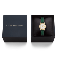 Daniel Wellingtonのネイビーのギフトボックスに収められたOphelia Mini Green Lizard White Guilloché Gold。クッションの上にゴールドケースとグリーンレザーストラップの腕時計が丁寧にセットされ、贈り物にぴったりの上品なパッケージです。