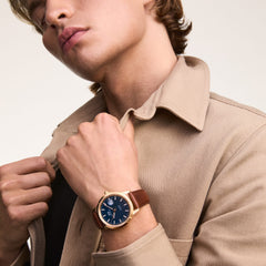 ベージュのジャケットの襟元に手を添える男性の手首に、Iconic St Mawes Automatic Rose Goldを着用しています。ブラウンのレザーストラップとローズゴールドケースが、落ち着いたトーンの装いに自然になじむデザインです。