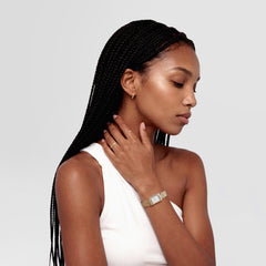 ダニエルウェリントン Arch Earrings Gold 9mmを着用したモデルの横顔です。白のノースリーブに合わせた小ぶりなゴールドのフープピアスが、耳元でさりげなく輝きを放ちます。ゴールドトーンの腕時計やリングと合わせることで、統一感のあるスタイリングを演出しています。