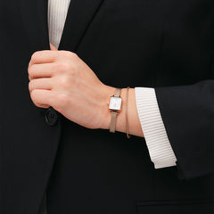 Tide Mesh Bracelet Melrose 1.8をローズゴールドのQuadro腕時計と重ね付けしたスタイリング例です。黒のジャケットと白のニットの袖口からのぞく手元に、細身のメッシュブレスレットが上品なアクセントを添えています。