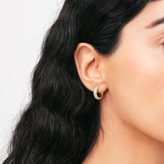 ダニエルウェリントン Pavé Crystal Earrings Goldを着用したモデルの耳元アップ。小ぶりなゴールドフープに敷き詰められたクリスタルが光を反射して輝き、耳たぶに自然になじむ様子が伝わります。