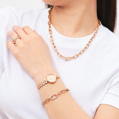 Daniel WellingtonのCrystal Link Ringローズゴールドを着用したスタイリング例。同コレクションのネックレスやブレスレット、腕時計とローズゴールドで統一し、白いトップスに映える華やかなコーディネートです。