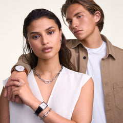 シルバーのCrystal Link Necklaceを着用した女性と男性のスタイリング例です。白いVネックトップスの胸元にシルバーリンクチェーンが映え、クリスタルリンクブレスレットや腕時計とのレイヤードコーディネートをお楽しみいただけます。