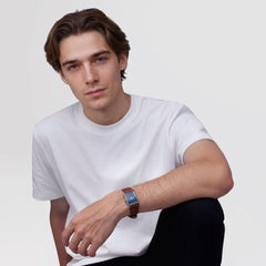 白いTシャツにダークパンツを合わせた男性が、Bound Light Brown Arctic Guilloché Silverを手首に着用している着用イメージです。ブルーのスクエアダイヤルとライトブラウンのレザーストラップが、カジュアルな装いに上品なアクセントを添えています。