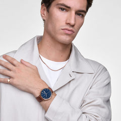 ライトグレーのジャケットに白Tシャツを合わせた男性が、Classic Day Display St Mawes Rose Gold Arcticを着用しています。ブルーの文字盤とブラウンのレザーストラップのコントラストが、カジュアルなスタイリングに落ち着いた存在感を添えています。