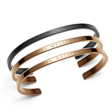 Daniel WellingtonのClassic Bracelet 3本セットは、マットブラック1本とポリッシュ仕上げのローズゴールド2本のオープンカフを組み合わせたミニマルデザインです。表面にはブランドロゴが刻印されています。