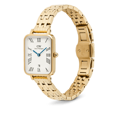 Daniel Wellington Quadro Roman Numerals Date 5-linkを斜めから撮影した画像です。ゴールドのポリッシュ仕上げ5リンクブレスレットとバタフライバックルのディテールが確認でき、ギョーシェ模様のホワイトダイヤルにブルーの針が映えるデザインとなっています。